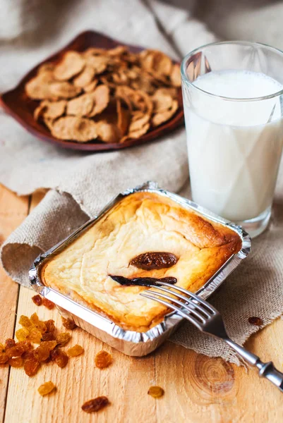 Güveç cottage cheese den ahşap bir masa üzerinde bir bardak süt ile bir fırında pişmiş. Peynirli incir üzerinden bir bardak süt ile kahvaltı için folyo pişirme için bir form ile.