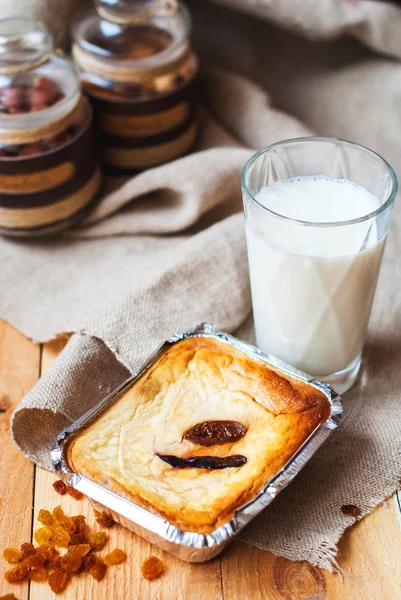 Casserole from cottage cheese baked in an oven with milk in a glass on a wooden table. Cheesecake with figs in a form for baking from foil for breakfast with a glass of milk. — Stock Photo, Image