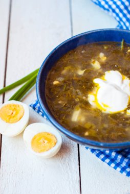 Yumurta beyaz ahşap zemin üzerine yeşil pancar çorbası. Kuzukulağı ve masmavi bir tabak ıspanak çorbası.