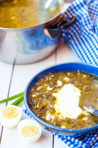 Зеленый борщ с яйцом на белом деревянном фоне. Суп из сорреля и шпината в глубокой синей тарелке . — стоковое фото