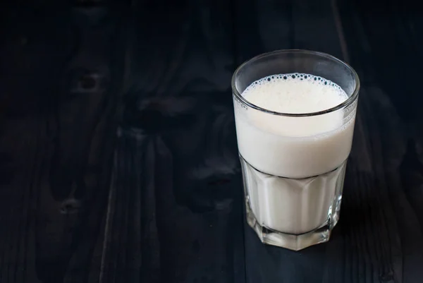 Un vaso de leche sobre un fondo oscuro. Leche en un vaso sobre una mesa de madera . —  Fotos de Stock