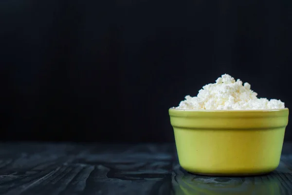 Just cottage cheese in ceramic ware on a dark background. Sour grainy cheese on a wooden table. — Stock Photo, Image