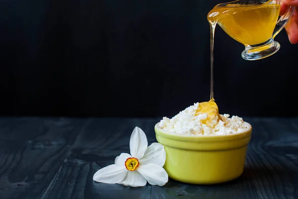 Den unga ost hälls med honung. Fräsch stuga ost och honung på en mörk bakgrund. Hand vatten honung med keso. — Stockfoto