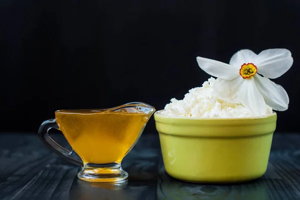 Fresh cottage cheese and honey. Honey and young cheese with a flower. Sour cheese in a deep plate and a glass jug with honey.