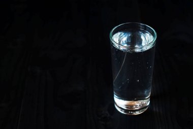 Sadece bir bardak su siyah bir arka plan. Koyu ahşap bir masa üzerinde bir bardak maden suyu.