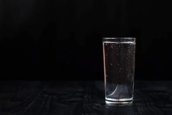 Just a glass of water on a black background. Mineral water in a glass on a dark wooden table.