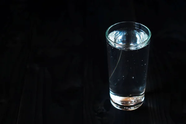 Just a glass of water on a black background. Mineral water in a glass on a dark wooden table.