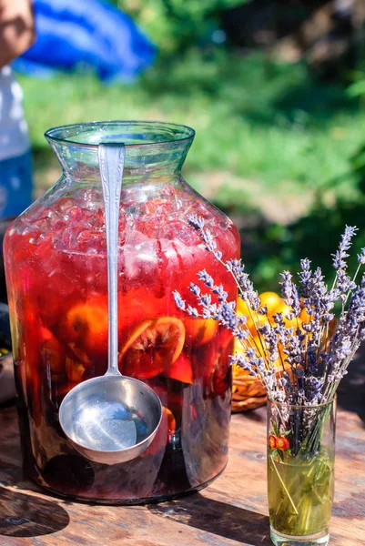 A large bottle of cold sangria with a ladle on the dacha table — Stock Photo, Image