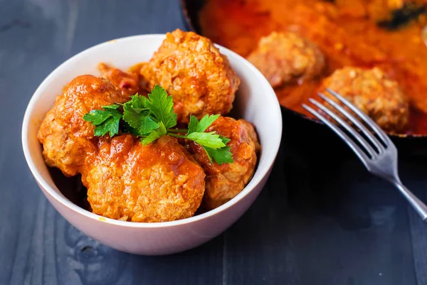 Derin bir tabak içinde yeşillikleri ile domates soslu köfte.