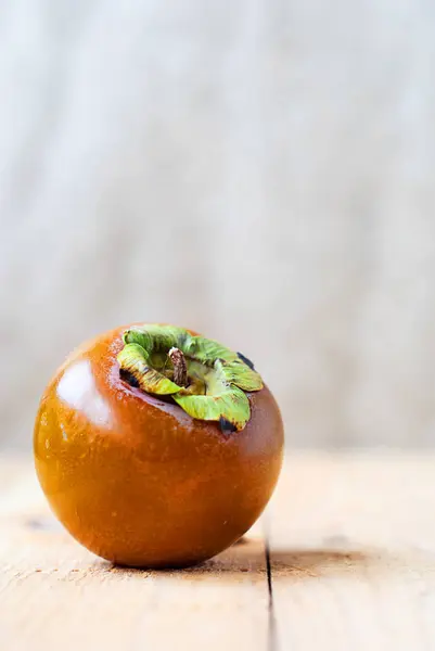 Chocolate persimmon crown on a light background and a wooden table. — Stock Photo, Image