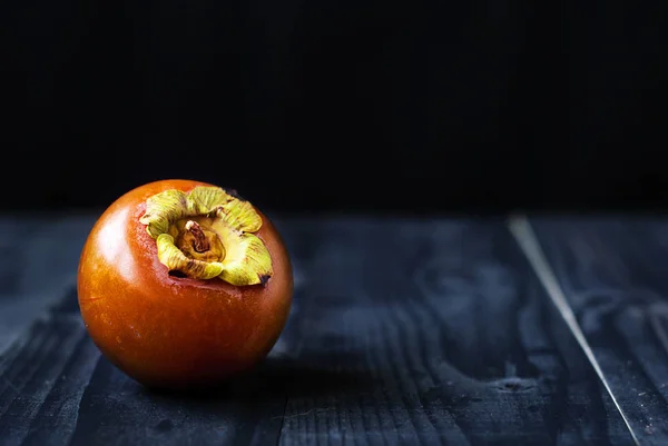 Chocolate persimmon on a black background and a wooden table. — Stock Photo, Image