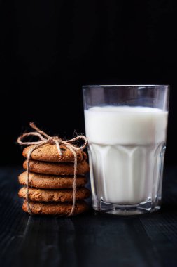 Yulaf ezmeli kurabiye kuru üzüm ve bir bardak süt için siyah arka plan üzerinde sağlıklı bir kahvaltı ile.