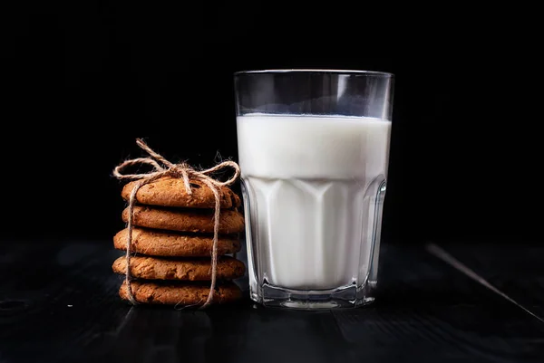 Havremjöl kakor med russin och ett glas mjölk för en hälsosam frukost på en svart bakgrund. — Stockfoto