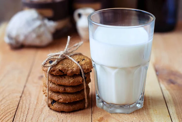 Colazione utile biscotti di farina d'avena con uva passa e un bicchiere di latte su un tavolo di legno . — Foto Stock