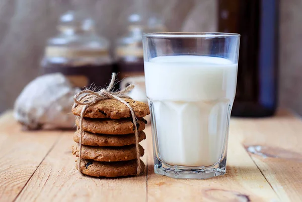 Colazione utile biscotti di farina d'avena con uva passa e un bicchiere di latte su un tavolo di legno . — Foto Stock