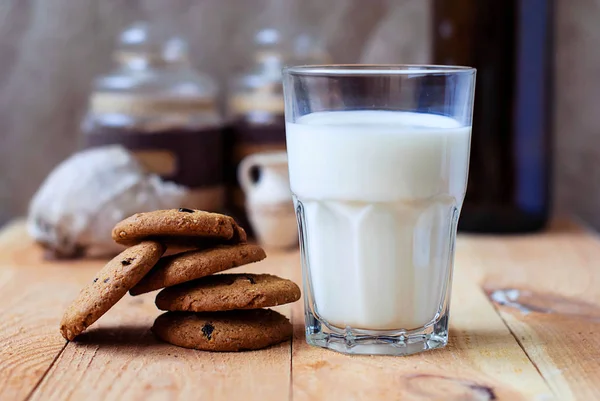 Colazione utile biscotti di farina d'avena con uva passa e un bicchiere di latte su un tavolo di legno . — Foto Stock