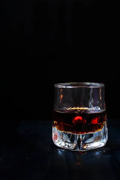 A glass of whiskey on a black background and a wooden table — Stock Photo, Image