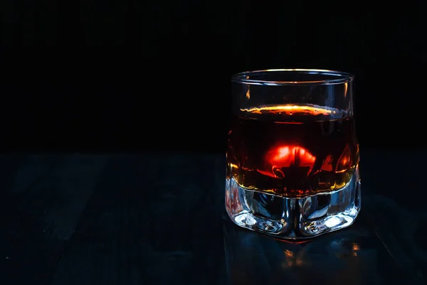 A glass of whiskey on a black background and a wooden table — Stock Photo, Image