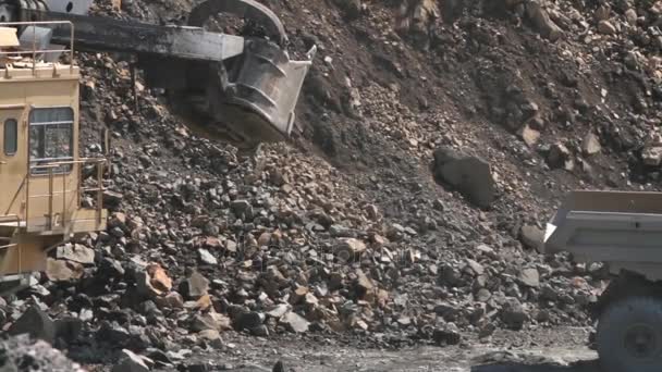 Экскаватор загружает камень в тяжелый грузовик в карьере, добывая гранит — стоковое видео