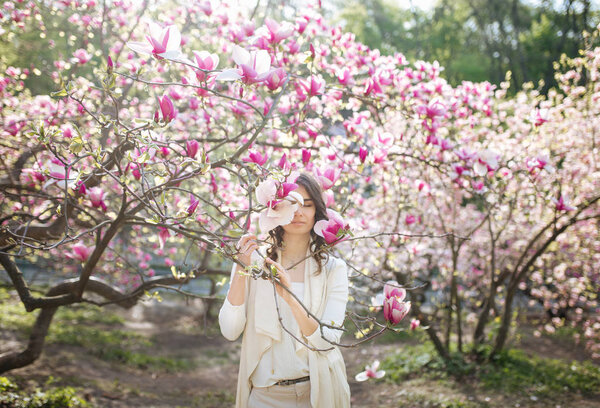 Beauty woman standing on Magnolia blossoming flowers background.