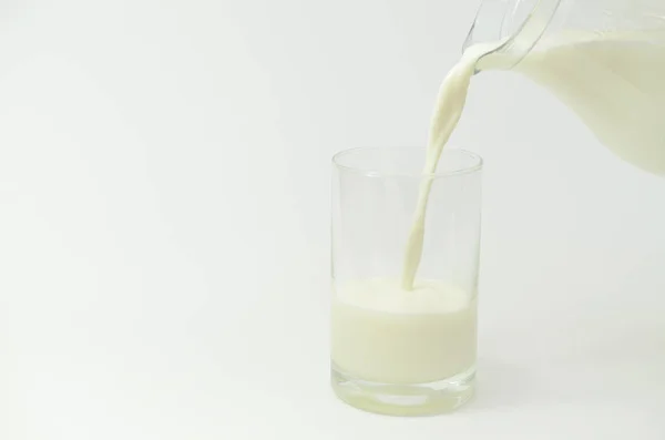 La leche en un frasco sobre un fondo claro se vierte en un vaso . — Foto de Stock