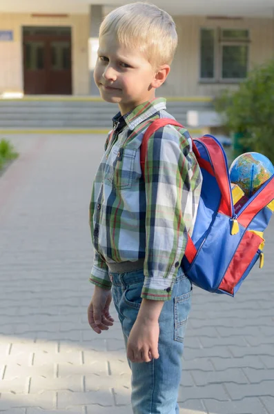 En pojke med en ränsel, böcker och en jordglob går till skolan efter en lång sommar. — Stockfoto
