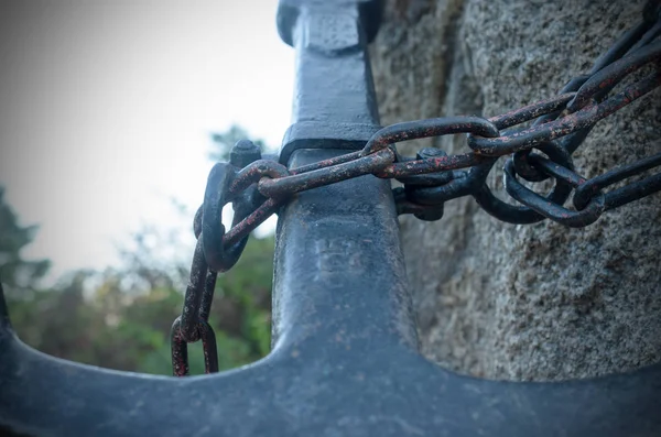 Uma estátua de uma grande âncora de metal, acorrentada a uma pedra . — Fotografia de Stock