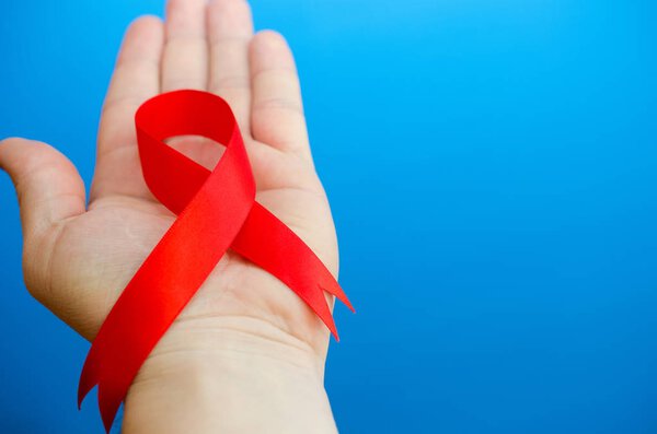 Red folded ribbon in hand on a blue background as a symbol of hemophilia.