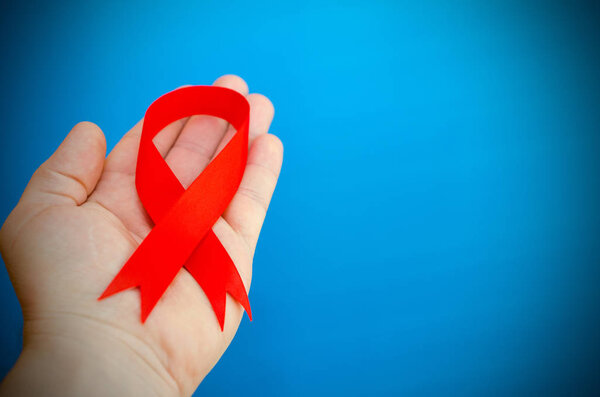 Red folded ribbon in hand on a blue background as a symbol of hemophilia.
