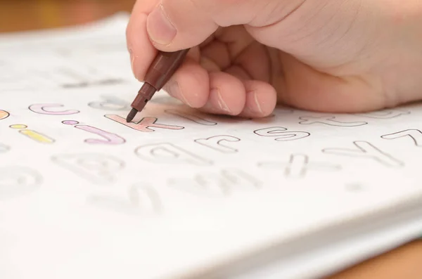 La mano de un niño escribe y muestra letras en inglés en un cuaderno y alfabeto con un lápiz y un rotulador . — Foto de Stock
