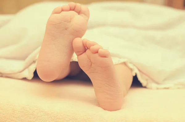 Детские ножки из-под одеяла на кровати . — стоковое фото