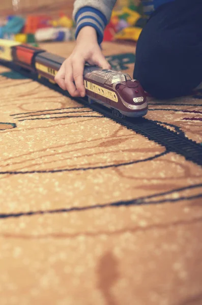 Sarışın bir çocuk halı üzerinde bir odada bir oyuncak tren ile çalış.