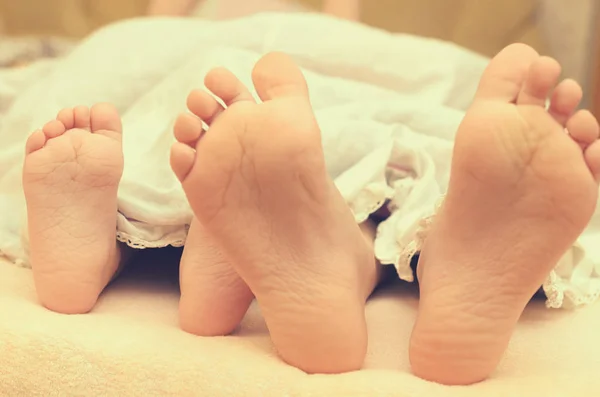 Baby feet from under the blanket on the bed.