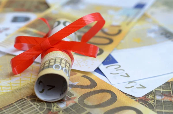 Rolls of money in a gift ribbon on bills of dollars and euros.