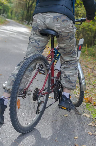 A girl in camouflage pants on a bicycle stands on the road.
