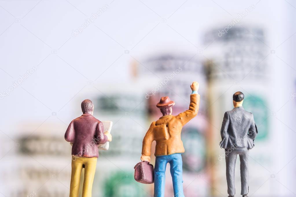 miniature figurine starring at big dollar banknotes