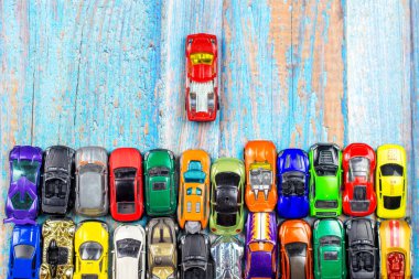 top view of many little car miniatures with one leader on wooden background clipart