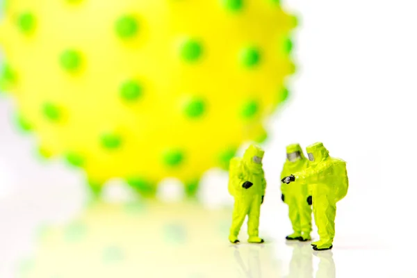 closeup of big corona virus with a team of special medical forces miniature figurines interfering during gas and other chemical accidents, the team preparing for diagnosis and action against very dangerous deadly virus type on white background