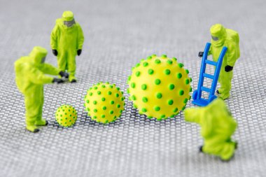 Büyük korona virüsüne yakın çekim. Özel tıbbi güçlerden oluşan bir ekip gaz ve diğer kimyasal kazalarda müdahale eden minyatür figürler. Ekip, gri arka planda yükselen çok tehlikeli ölümcül virüse karşı teşhis ve eyleme hazırlanıyor. 