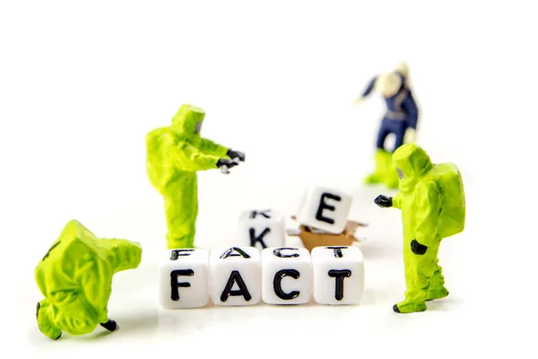 fake and fact text formed of white dices with black letters and little miniature figurines of workers on white background, how can you distinguish between credible information and fake news, critical thinking