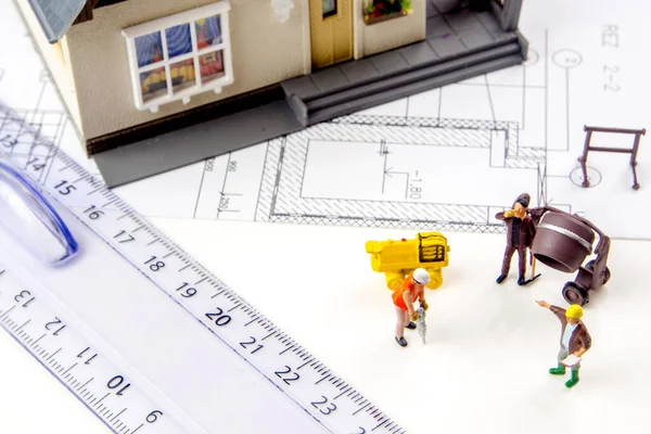 closeup of small miniature plastic house with  miniature figurine workers and constructing plans