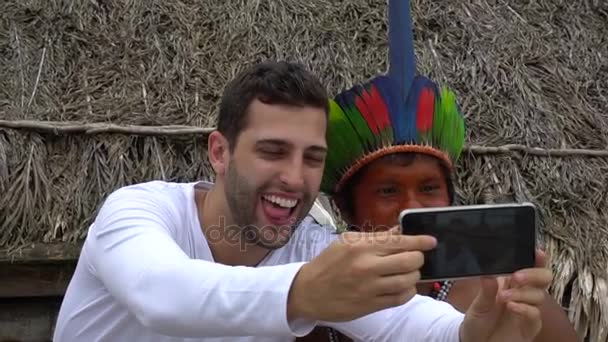 Turista che si fa un selfie con un nativo brasiliano - uomo indigeno - in una tribù Tupi Guarani, Brasile — Video Stock