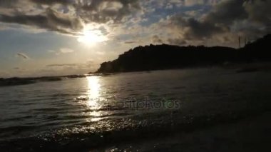 Kumlu sahilde günbatımı sırasında yürüyen kadın