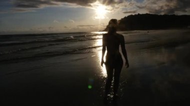 Kumlu sahilde günbatımı sırasında yürüyen kadın