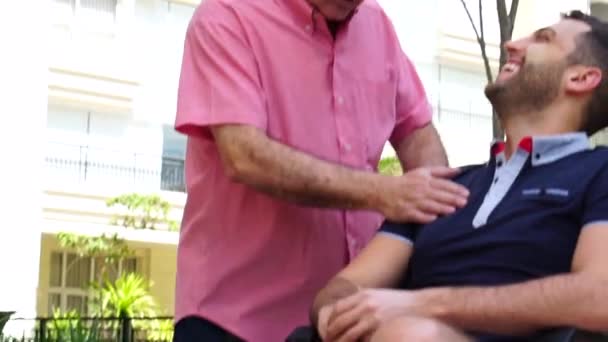 Отец поощряет своего сына-инвалида в инвалидном кресле в парке — стоковое видео