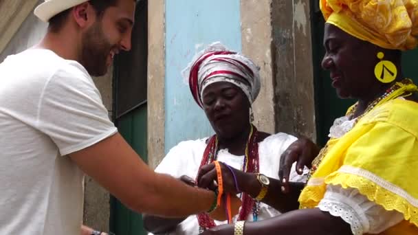 Baianas Acolhendo o Turista dando algumas "Fitas de Desejo Brasileiras" em Salvador, Brasil - as fitas são consideradas amuletos de boa sorte — Vídeo de Stock