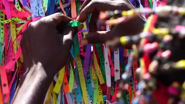 Brézilien faisant un vœu avec des rubans brésiliens (Fita do Bonfim) sur la clôture de l'église à Salvador, Bahia, Brésil — Video