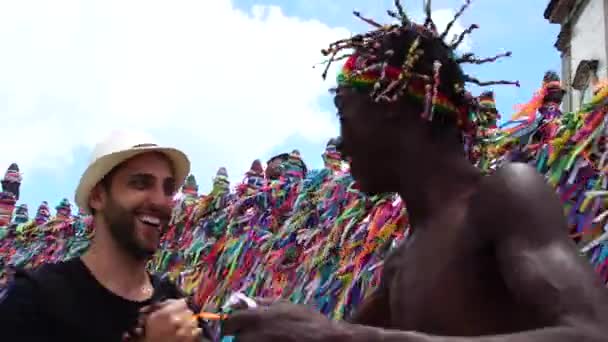 Hombre brasileño dando la bienvenida al turista dando algunas "cintas de deseos brasileños" en Salvador, Brasil - las cintas se consideran encantos de buena suerte — Vídeos de Stock