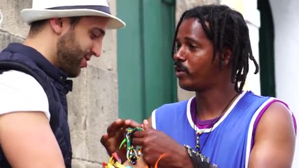 Vendedor de rua recebe turista dando algumas fitas brasileiras (Fita do Bonfim) em Salvador, Bahia, Brasil — Vídeo de Stock