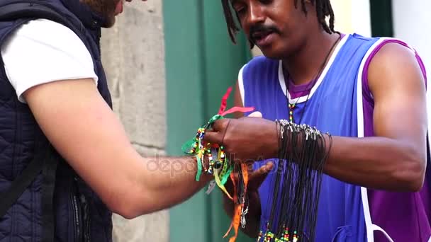 Pouliční dodavatel příjemné turistické dává některé brazilské stužky (Fita do Bonfim) na v Salvadoru, Bahia, Brazílie — Stock video